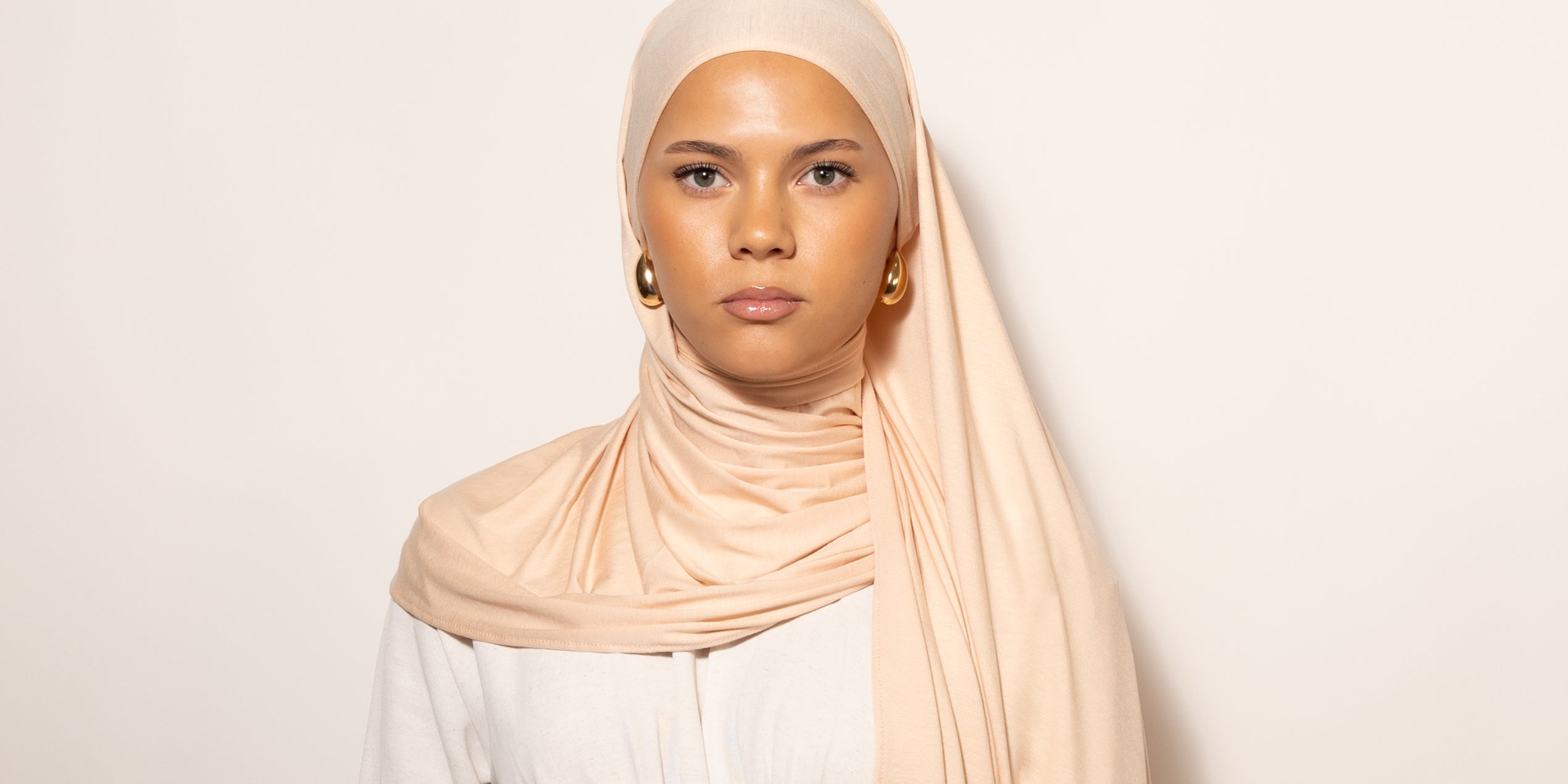 Nainen katsoo kameraan puettuna tyylikkääseen vaaleaan Hijab huiviin